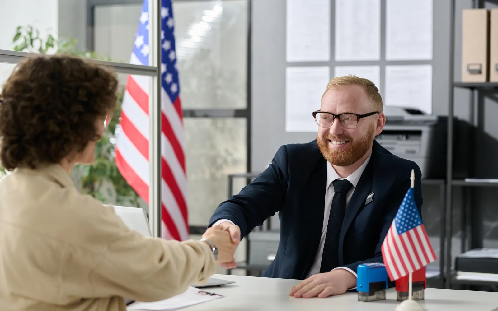 Attorney shaking hands with a client in an office with American flags