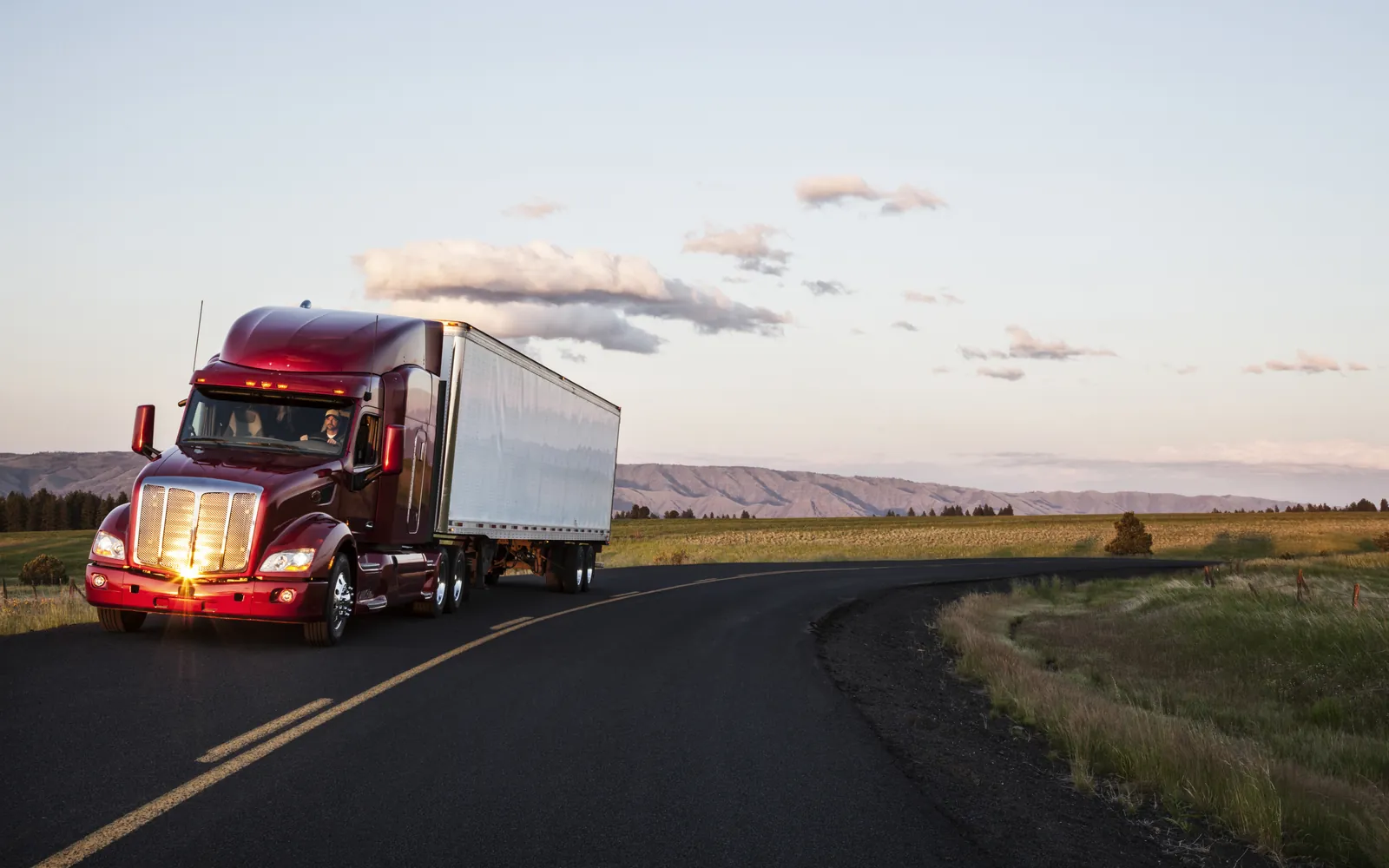 Red semi-truck hauling freight on a US highway at golden hour